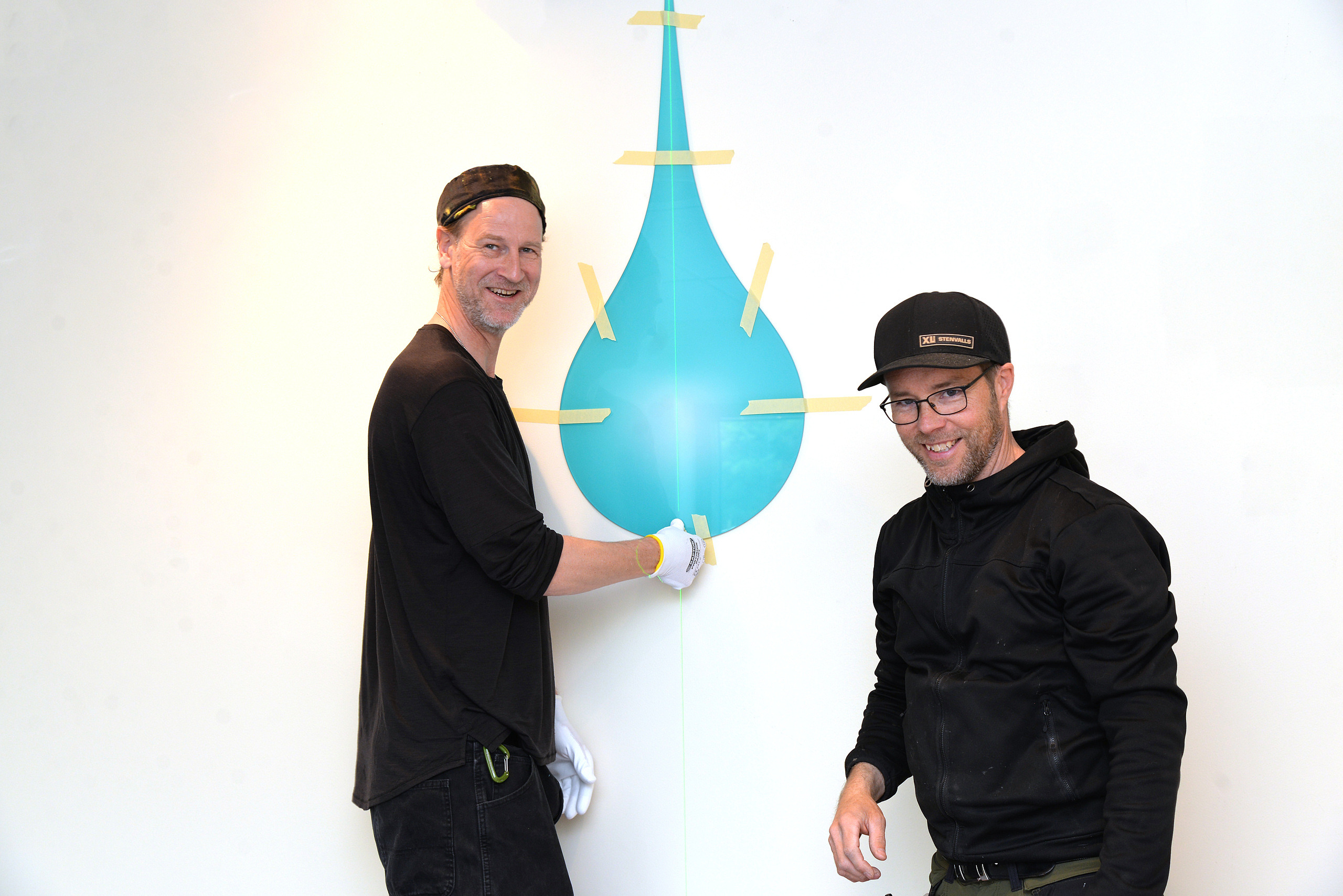 Martin Kallin och Tomas Edin hjälper konstnären Maria Bajt att sätta upp konstverken i nya sport- och simhallen.