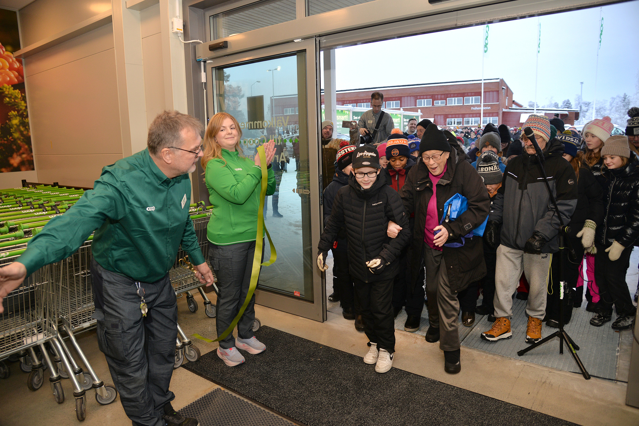 Ulf hälsar välkommen in ny nya Coop-butiken, 2025-11-22, Coops butikchef Ulf Isaksson, klippper invigningsbandet, och hälsar den långa kön välkommen in i nya butiken.