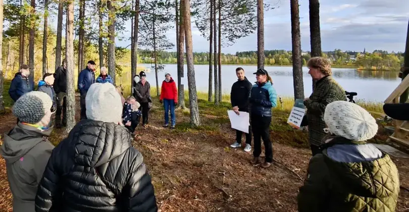 En grupp människor som stor i en cirkel i skogen och en av de talar